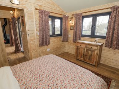 A bedroom with floral bedspread wooden chest of drawers and patterned curtains at Willow in Dunchurch