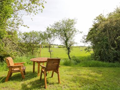 A wooden table with two chairs on grass near trees overlooking a green field at Willow in Dunchurch
