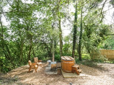 An outdoor area with two wooden chairs a wooden hot tub with steps a metal stove and trees surrounding the space at Willow in Dunchurch