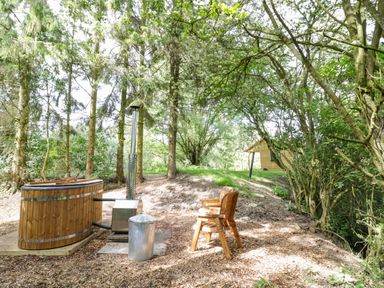 An outdoor setting with a wooden hot tub a metal chimney pipe two wooden chairs trees and a wooden cabin in the background at Willow in Dunchurch
