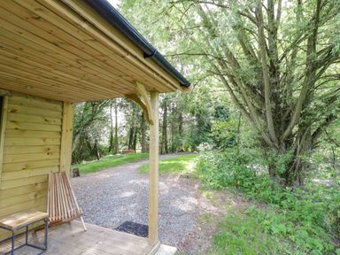 A wooden porch with a chair and small table next to a gravel pathway and trees at Willow in Dunchurch