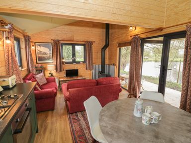 A living room with red sofas a small television and a round dining table with cups and a teapot at Willow in Dunchurch