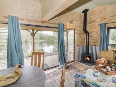 A room with wood burning stove table chairs and large windows overlooking a lake at Dragonfly in Dunchurch