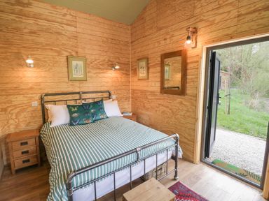 A bedroom with a metal bed frame striped duvet and butterfly pillow bedside tables wooden walls and an open door leading outside at Dragonfly in Dunchurch