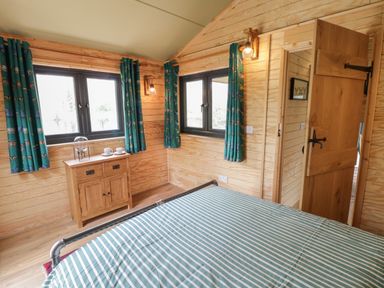 A bedroom with wooden walls bed with striped bedding two windows with patterned curtains and a wooden cabinet at Dragonfly in Dunchurch