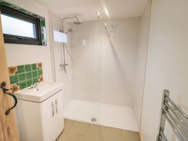 A bathroom with a shower area, sink with cabinet, window, and towel radiator at Dragonfly in Dunchurch