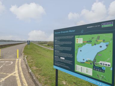 A pathway along a reservoir with a map and information board about Draycote Water in Dunchurch