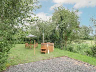 An outdoor garden with a wooden hot tub table with umbrella chairs and trees at Dragonfly in Dunchurch