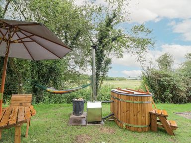 An outdoor garden area with a wooden hot tub a hammock and a wooden table with an umbrella at Dragonfly in Dunchurch