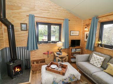 A living room with a wood stove a gray couch blue curtains and a tray on a ottoman at Dragonfly in Dunchurch