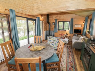 An open-plan living space with a dining table and chairs a sofa a wood-burning stove and kitchen appliances at Dragonfly in Dunchurch