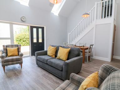 A living area with a gray sofa and two plaid armchairs with yellow cushions a wooden dining table with chairs under stairs at Willow Cottage in Combe Martin