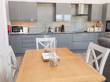 A kitchen with grey cabinets a wooden dining table with chairs and glass vases filled with pebbles at Willow Cottage in Combe Martin