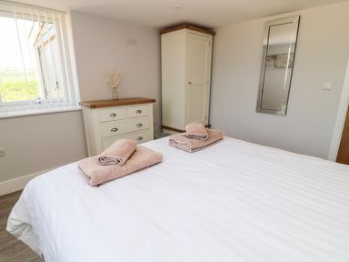 A bedroom with a bed and folded towels two cabinets and a mirror on the wall at Willow Cottage in Combe Martin