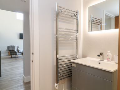 A bathroom with a grey vanity unit a white sink a chrome towel radiator and a mirror with lights at Willow Cottage in Combe Martin