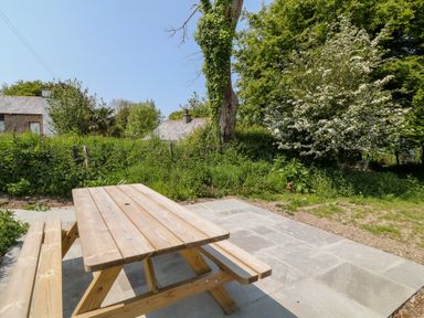 An outdoor wooden picnic table on a stone patio with trees and houses in the background at Willow Cottage in Combe Martin