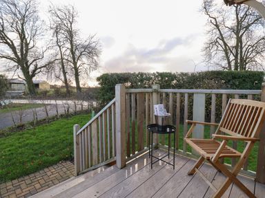A wooden deck with a chair and a small table with a bucket on it overlooking a garden at Arts and Crafts in Bolton Percy near Tadcaster