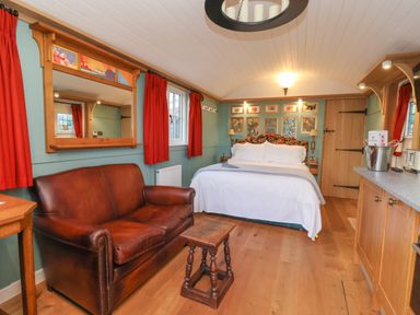 A bedroom with a double bed a brown leather sofa a small wooden table and red curtains at Arts and Crafts in Bolton Percy near Tadcaster