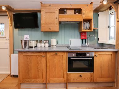 A kitchen with wooden cabinets a stove a sink a kettle and a television on the wall at Arts and Crafts Bolton Percy near Tadcaster