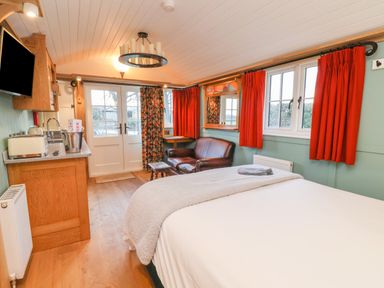 A room with a bed a small kitchen area a leather sofa a wooden floor and red curtains at Arts and Crafts Bolton Percy near Tadcaster