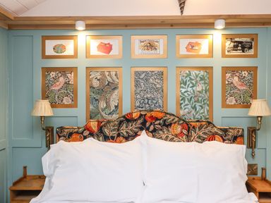 A bed with white pillows and a patterned headboard under framed pictures on a blue wall at Arts and Crafts Bolton Percy near Tadcaster