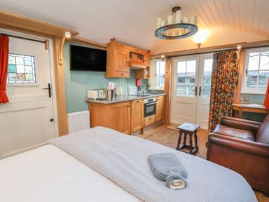 A small living space with a bed, kitchen area, television, leather sofa, and windows at Arts and Crafts in Bolton Percy near Tadcaster