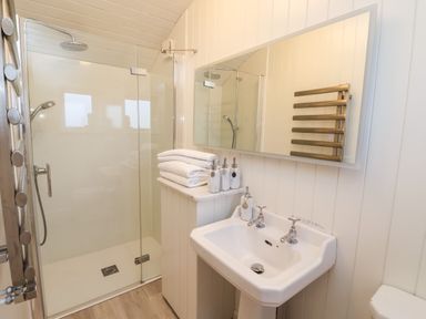 A bathroom with a glass shower enclosure towels on a shelf a sink with soap dispensers and a mirror at Arts and Crafts in Bolton Percy near Tadcaster