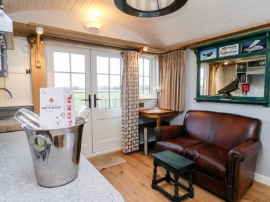 A small living area with a brown leather sofa a wooden stool a corner table with a lamp and double glass doors leading outside at Amy Johnson in Bolton Percy near Tadcaster