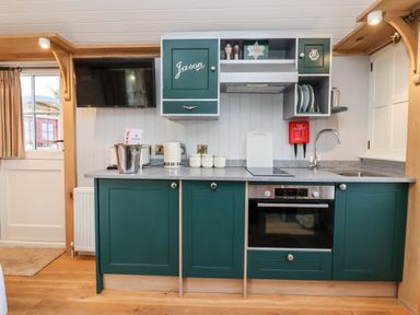 A kitchen with green cabinets a sink an oven a TV and kitchen utensils at Amy Johnson in Bolton Percy near Tadcaster