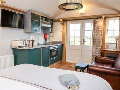 A kitchen area with green cabinets a sink an oven a television and a wooden chair near glass doors at Amy Johnson Bolton Percy near Tadcaster