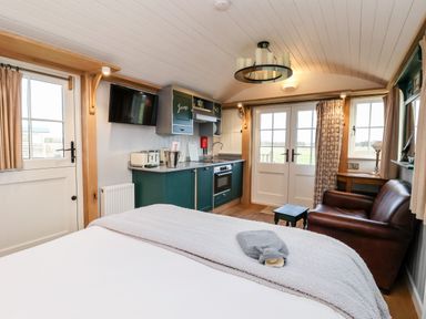 A room with a bed kitchen cabinets a leather sofa and French doors at Amy Johnson in Bolton Percy near Tadcaster