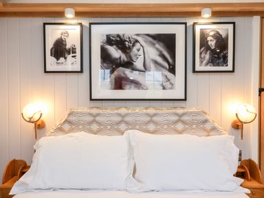 A bedroom with a patterned headboard two white pillows three black and white portraits and two wall lamps at Amy Johnson Bolton Percy near Tadcaster