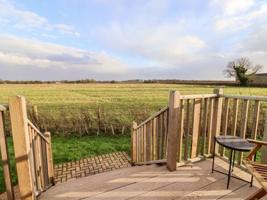 A wooden deck with stairs and a small round table overlooking a grassy field with sheep at Amy Johnson in Bolton Percy near Tadcaster