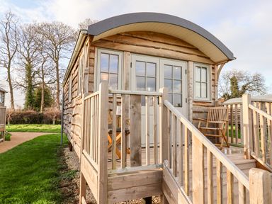 A wooden cabin with a curved roof and a small porch with railings and chairs at Amy Johnson in Bolton Percy near Tadcaster