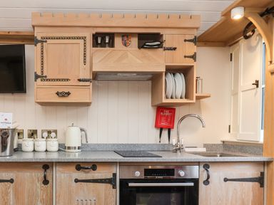 A kitchen with wooden cabinets a countertop with a kettle and jars a sink a faucet an oven and plates at The White Princess Bolton Percy near Tadcaster