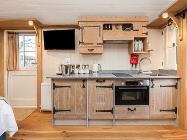 A kitchen with wooden cabinets, a sink, oven, kettle, toaster, and a mounted television at The White Princess in Bolton Percy near Tadcaster