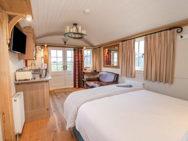 A bedroom with a bed a leather sofa a wall mirror curtains and a kitchenette at The White Princess in Bolton Percy near Tadcaster