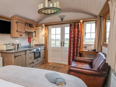 A compact kitchen with wooden cabinets next to a brown leather sofa and double doors with a window at The White Princess Bolton Percy near Tadcaster