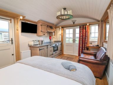 A room with a kitchen area, a leather armchair, a bed, and double doors with windows at The White Princess in Bolton Percy near Tadcaster