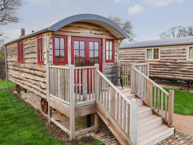 A wooden hut with red windows and door on a small wooden deck with stairs on grass