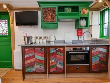 A kitchen with multicolored cabinet doors green upper cabinets a sink a stovetop an oven a TV mounted on the wall and a green door with stained glass at Folklore Bolton Percy near Tadcaster