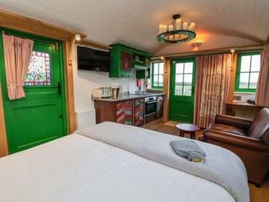 A room with a bed a kitchen area green doors and windows and a brown leather armchair at Folklore in Bolton Percy near Tadcaster