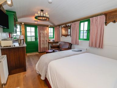 A bedroom with a bed a brown leather sofa a green door and windows and a kitchenette at Folklore in Bolton Percy near Tadcaster