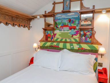A bedroom with a bed and colorful headboard featuring a landscape design and wall-mounted lamps at Folklore in Bolton Percy near Tadcaster