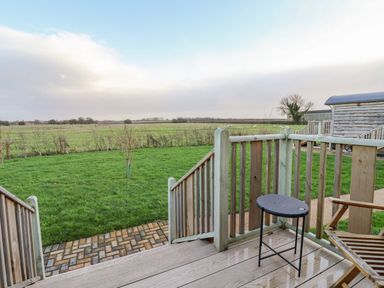 A wooden deck with a small table and chair overlooking a green lawn and open field at Folklore in Bolton Percy near Tadcaster