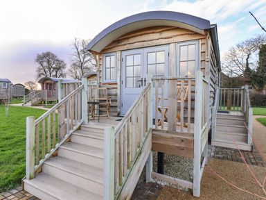 A small wooden cabin with steps leading to a porch with chairs and a table at The Fenton in Bolton Percy near Tadcaster