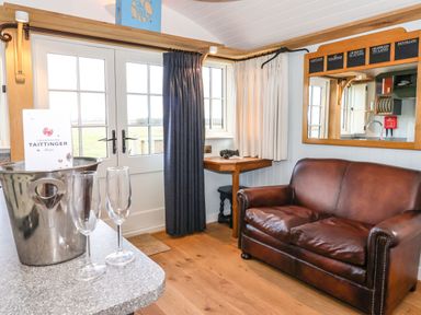 A room with a brown leather sofa a small wooden table and a window with dark and white curtains at The Fenton in Bolton Percy near Tadcaster