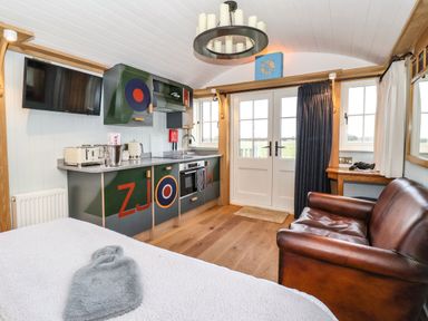 A small kitchen with cabinets and appliances next to a brown leather sofa and white double doors at The Fenton in Bolton Percy near Tadcaster