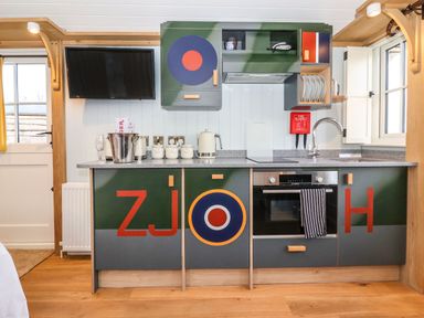 A kitchen with green and gray cabinets with large red letters a wall mounted television and a countertop with kettle and canisters at The Fenton in Bolton Percy near Tadcaster