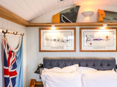 A bedroom with a grey upholstered headboard two framed airplane prints and flags hanging on a wall at The Fenton in Bolton Percy near Tadcaster
